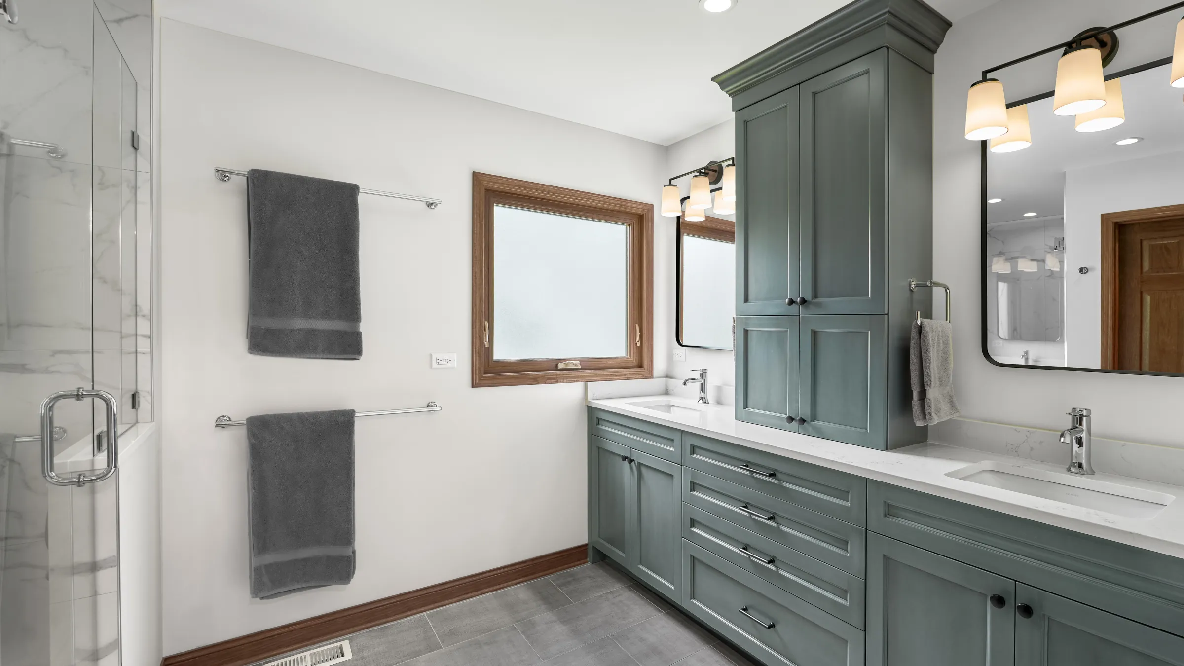 Modern primary bathroom with gray shaker cabinets, white quartz countertops, dual sinks, and a glass shower.