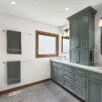 Modern primary bathroom with gray shaker cabinets, white quartz countertops, dual sinks, and a glass shower.