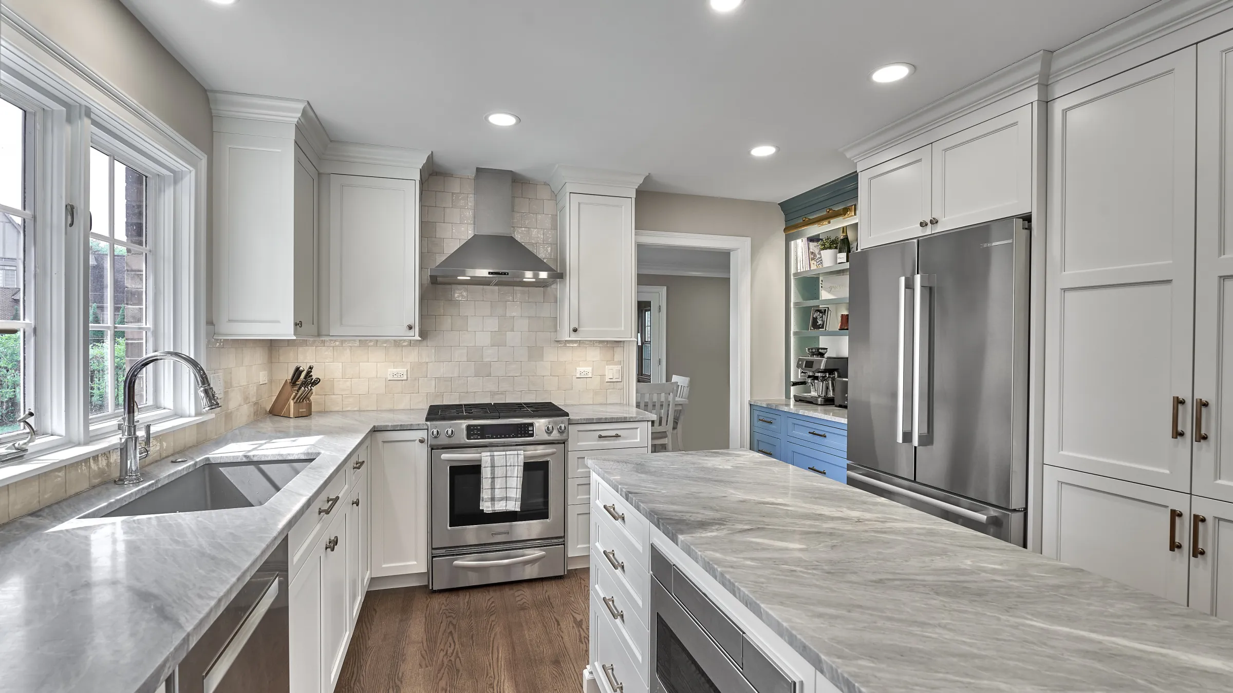 Modern kitchen remodel featuring white shaker cabinets, gray marble countertops, stainless steel appliances, and wood floors.