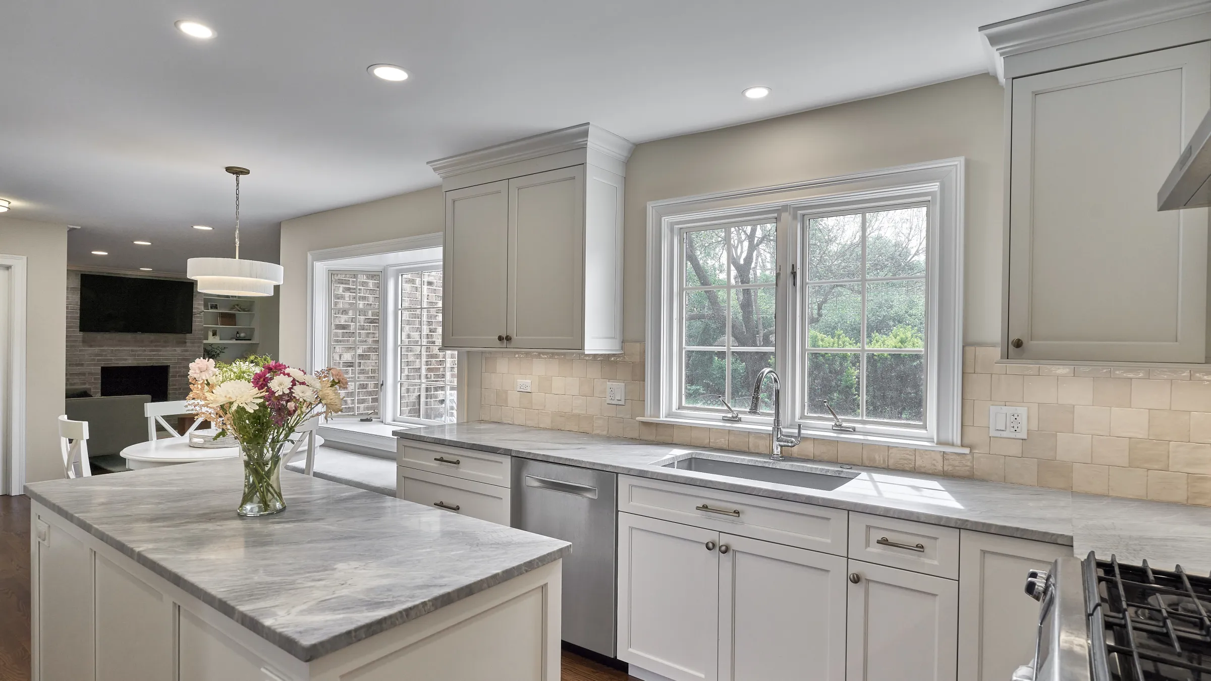 Bright, modern kitchen remodel with white shaker cabinets, gray marble countertops, stainless steel appliances, and large win