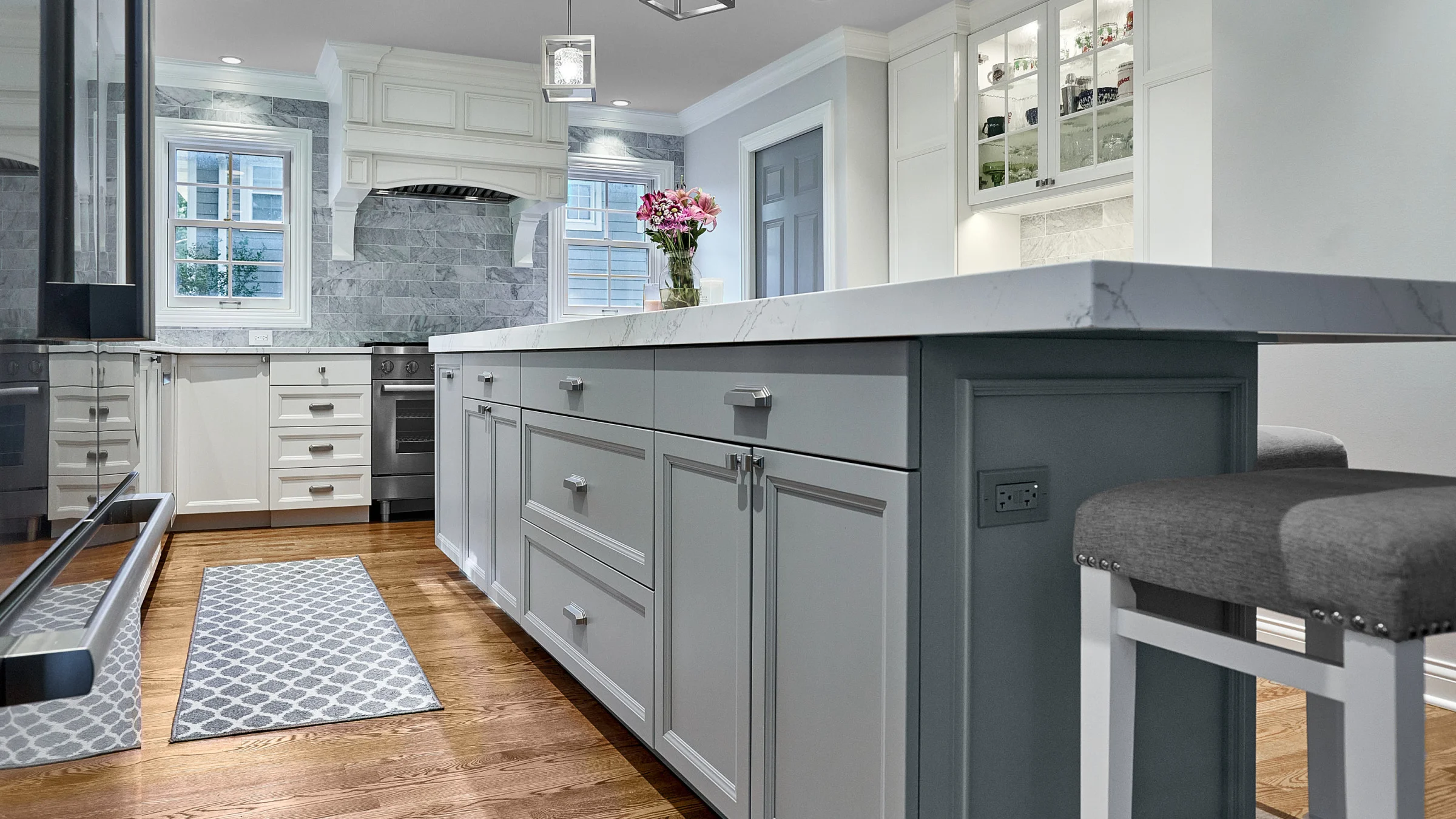 Arlington Heights kitchen remodel featuring a gray island, white cabinets, marble countertops, wood floors, and stylish accen