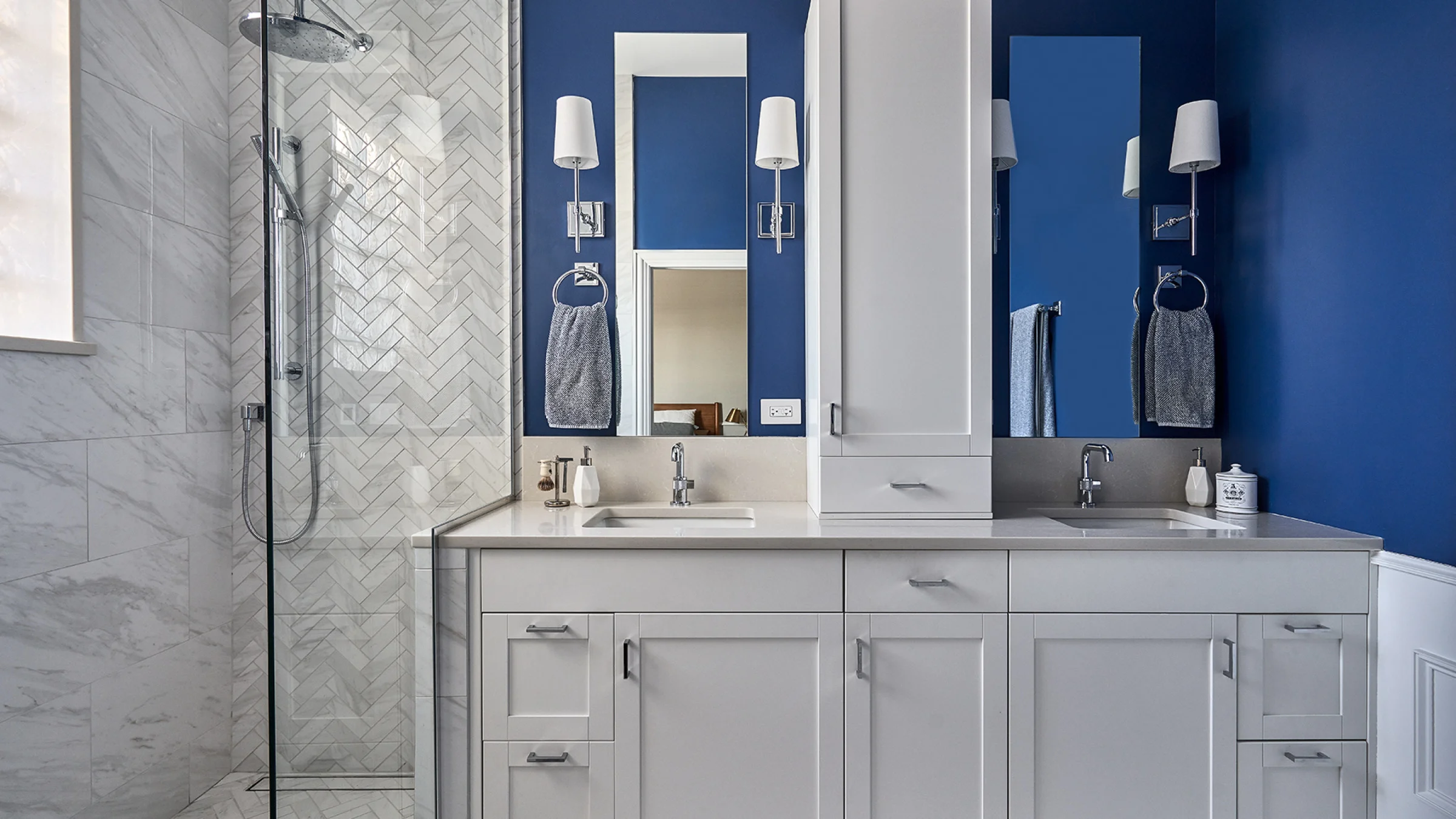 Chicago bathroom remodel: double vanity with white cabinets, blue walls, herringbone tile shower, modern lighting.